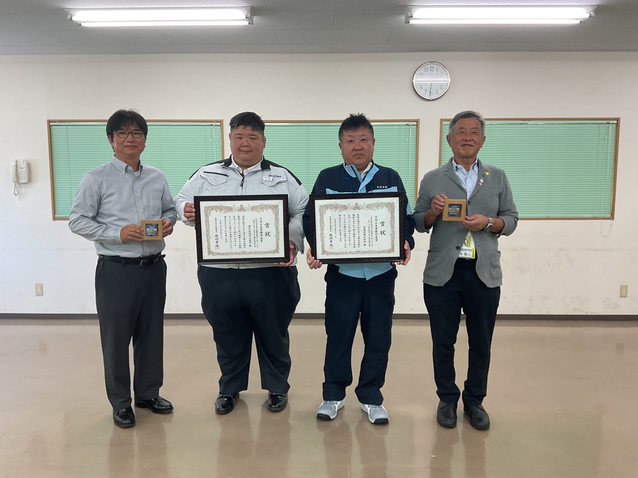 日向土木事務所長賞の表彰状と盾を手に並ぶ受賞者4人。中央の2人が額に入った表彰状を、両端の2人が盾を持っている
