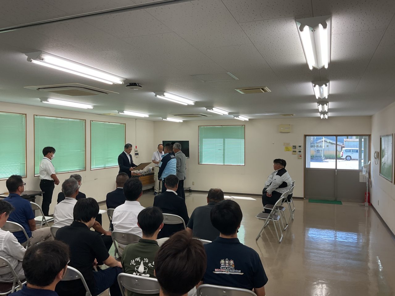 表彰式の会場。着席した出席者が見守るなか、会場前方で表彰状が手渡されている