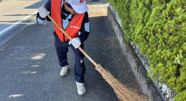 竹ぼうきで路肩を掃き上げる社員