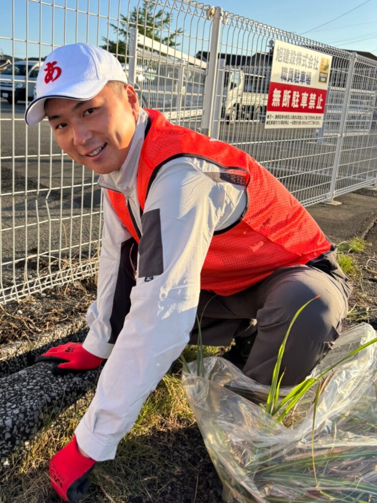 当社駐車場のフェンス沿いで、刈った草を袋に詰める社員